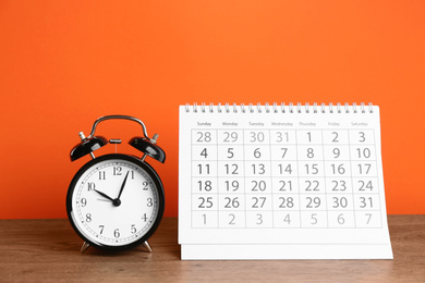 Calendar and alarm clock on wooden table against orange background