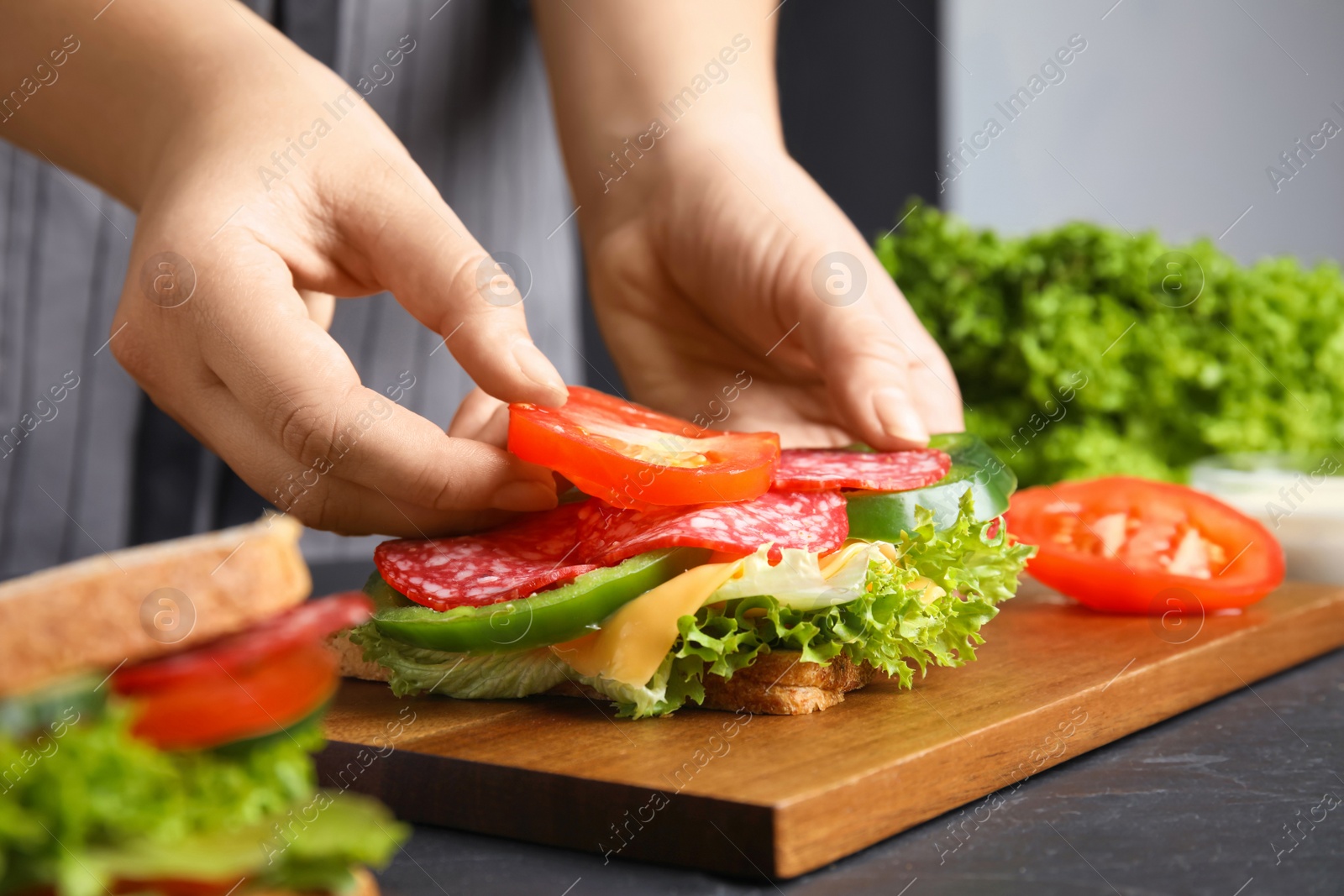 Photo of Woman adding tomato to sandwich at black table, closeup