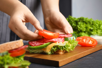 Photo of Woman adding tomato to sandwich at black table, closeup