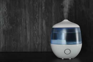 Modern air humidifier on table against wooden background. Space for text
