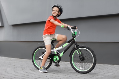 Little boy riding bicycle on street near gray wall