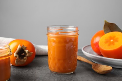Photo of Delicious persimmon jam in glass jar served on gray table