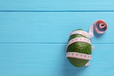 Photo of Healthy diet. Avocado and measuring tape on light blue wooden table, top view. Space for text