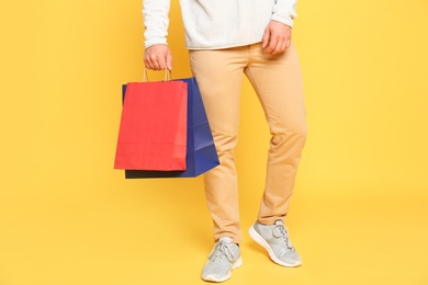 Young man with paper bags on yellow background, closeup