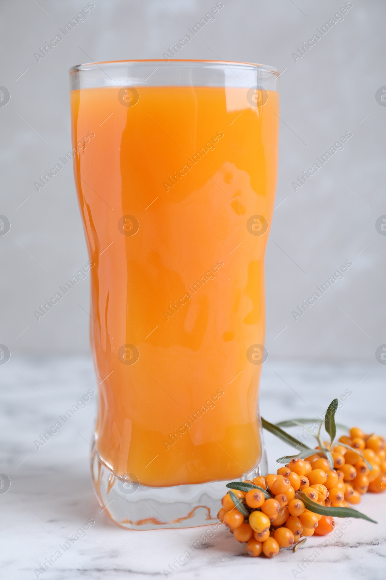 Photo of Delicious sea buckthorn juice and fresh berries on white marble table against grey background