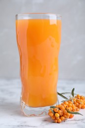 Delicious sea buckthorn juice and fresh berries on white marble table against grey background