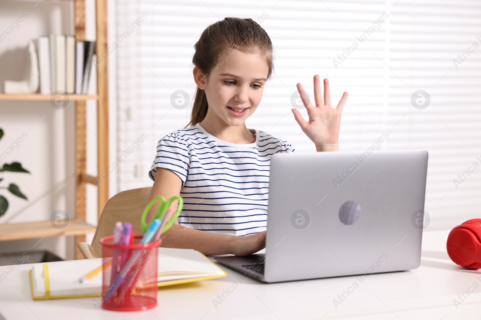 Photo of E-learning. Cute girl raising her hand to answer during online lesson at table indoors