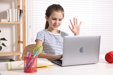 E-learning. Cute girl raising her hand to answer during online lesson at table indoors