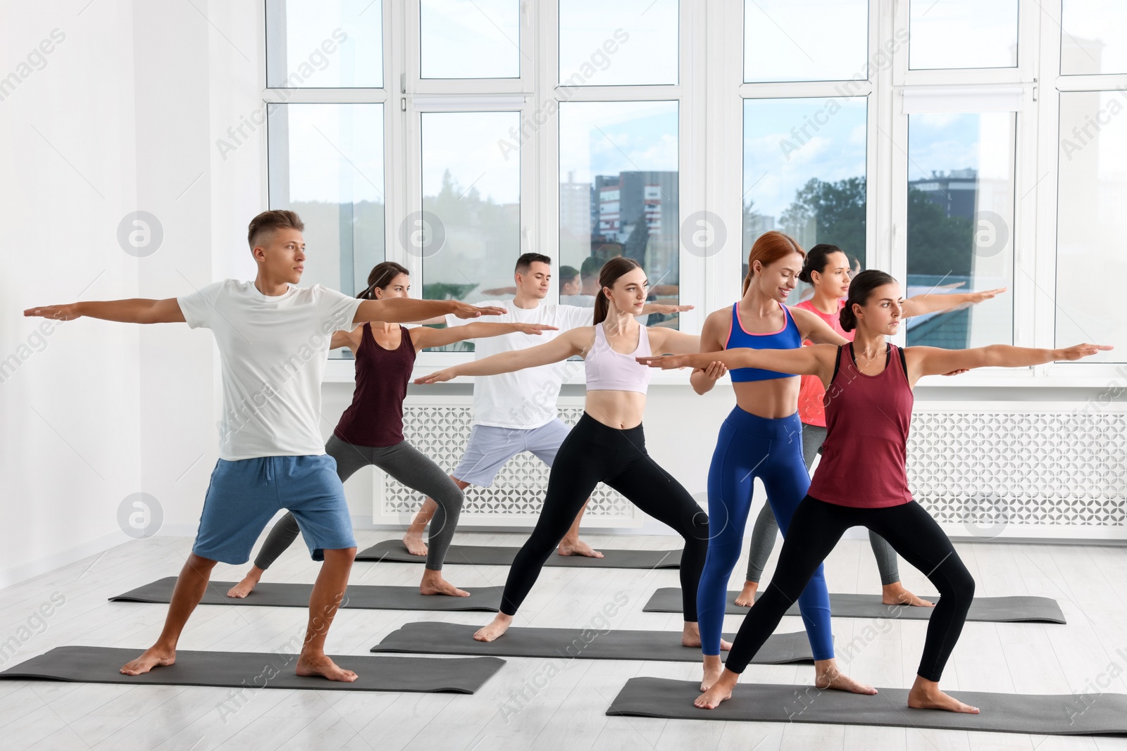 Photo of Yoga coach helping woman during group lesson indoors