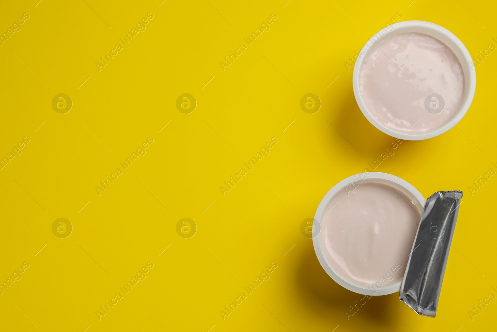 Photo of Plastic cups with tasty yogurt on yellow background, flat lay. Space for text