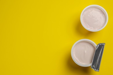 Photo of Plastic cups with tasty yogurt on yellow background, flat lay. Space for text