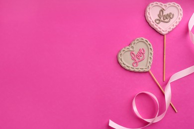 Photo of Chocolate heart shaped lollipops and ribbon on pink background, flat lay. Space for text