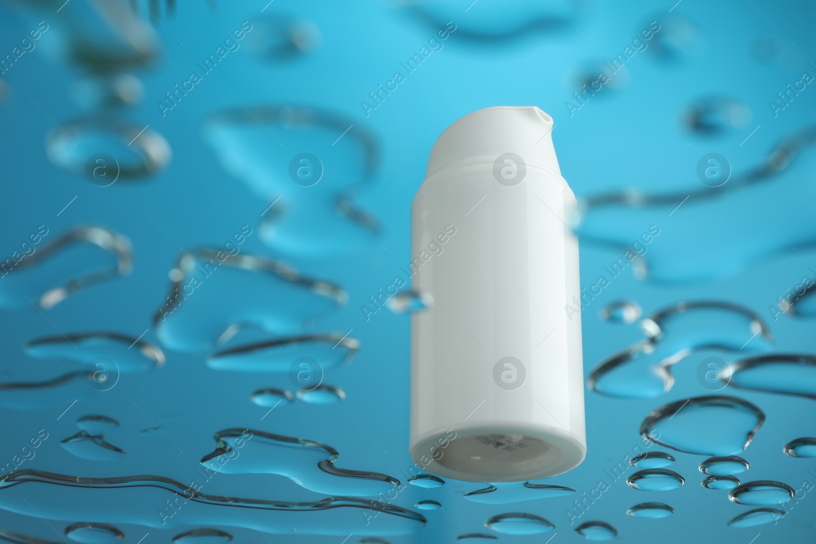 Photo of Moisturizing cream in bottle on glass with water drops against blue background, low angle view. Space for text