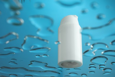 Photo of Moisturizing cream in bottle on glass with water drops against blue background, low angle view. Space for text