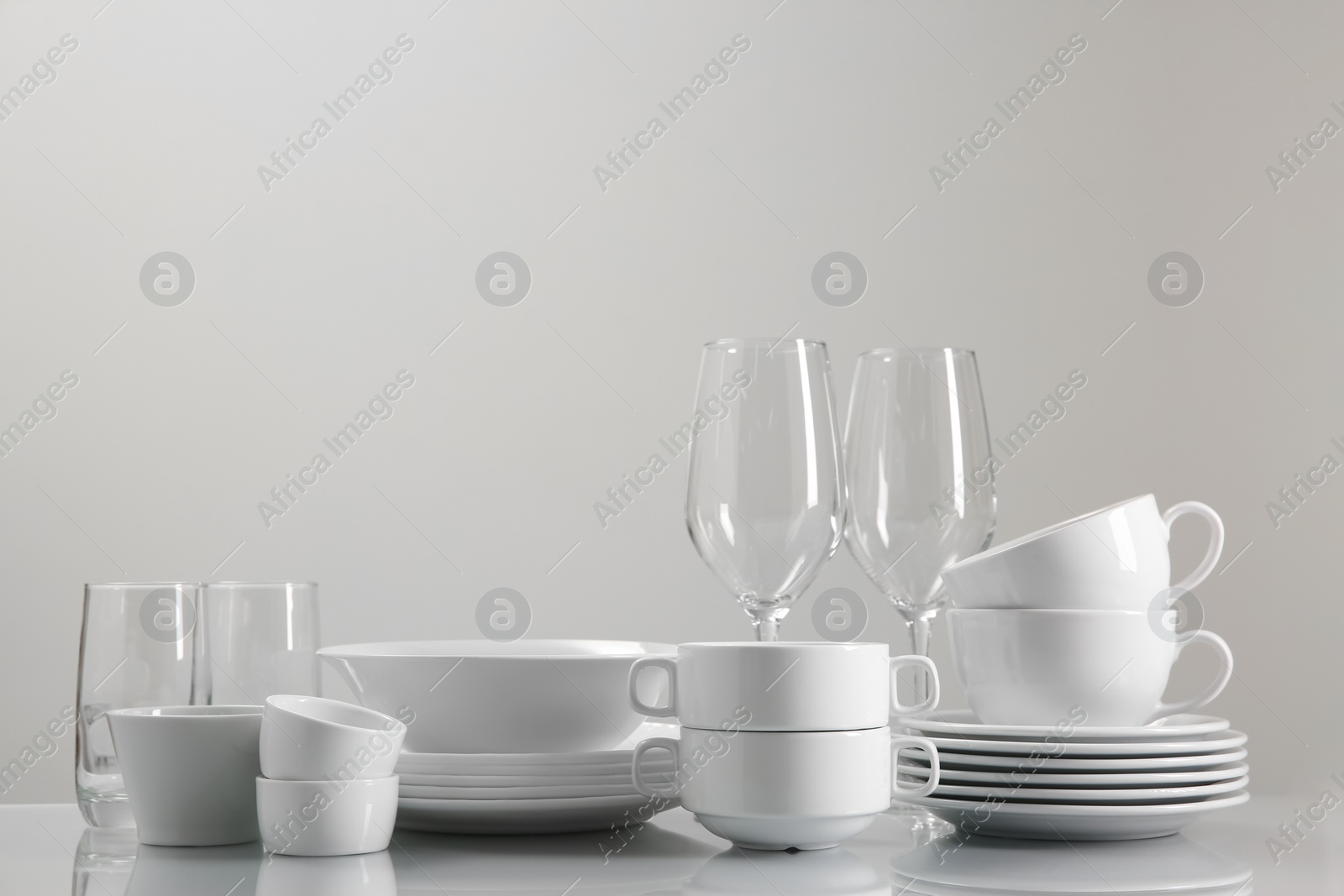 Photo of Set of many clean dishware and glasses on light table. Space for text