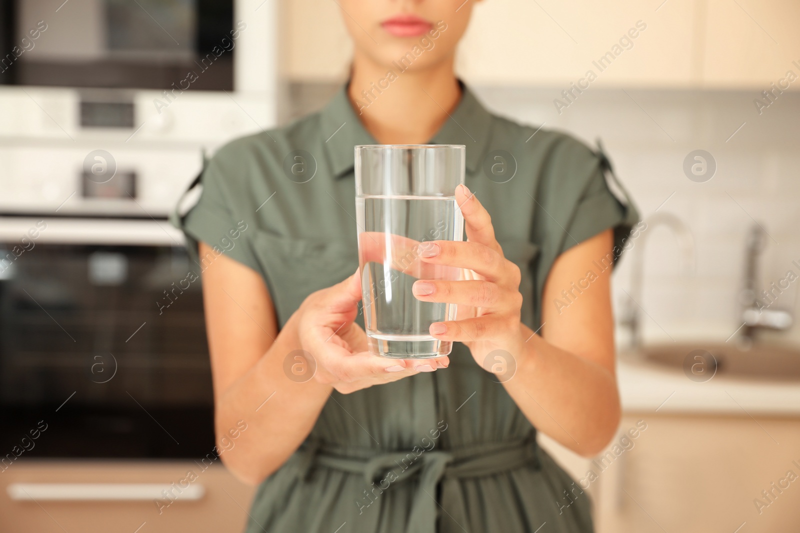 Photo of Woman holding glass with pure water in kitchen, closeup