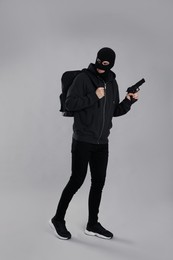 Photo of Man wearing black balaclava with backpack and gun on light grey background