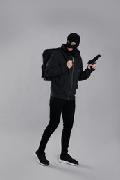 Man wearing black balaclava with backpack and gun on light grey background