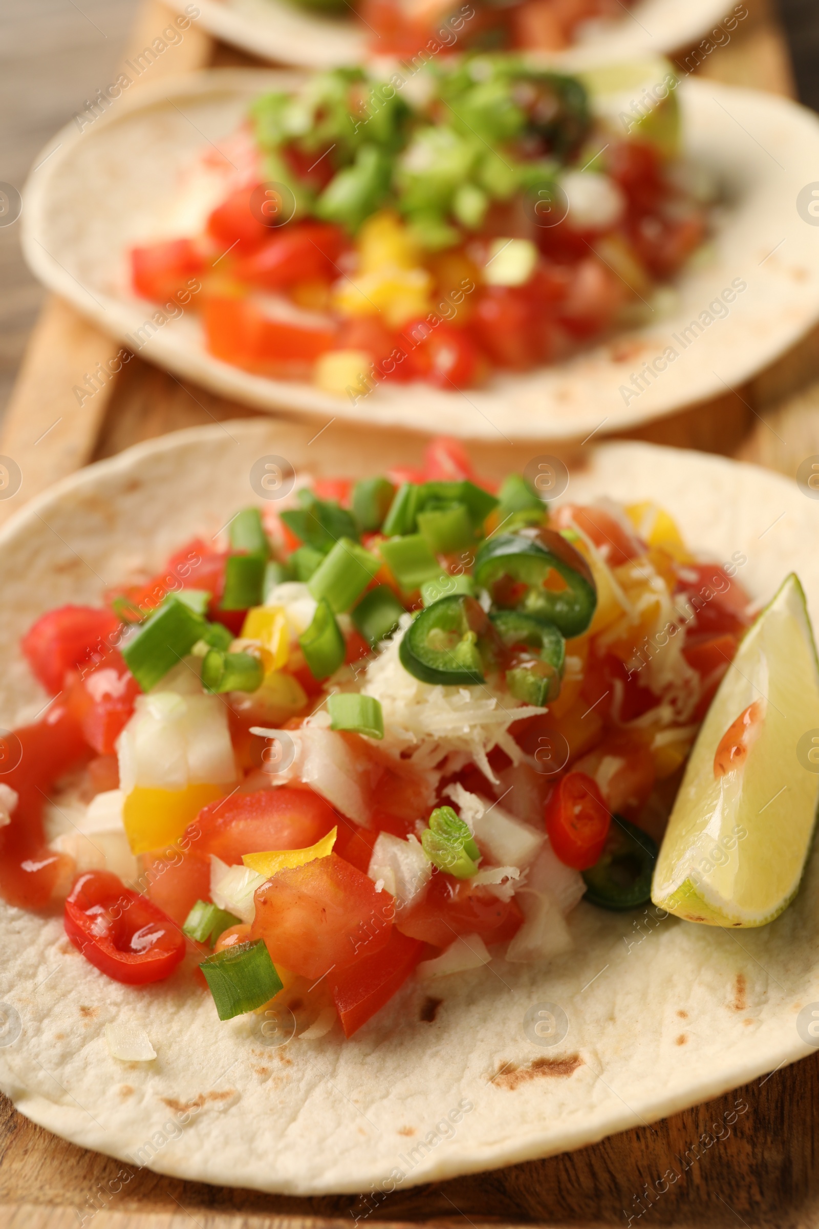 Photo of Delicious tacos with vegetables, green onion, lime and ketchup on table, closeup