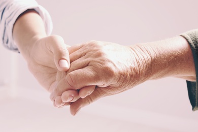 Photo of Woman holding hands with senior lady on light background, closeup. Elderly care and help concept