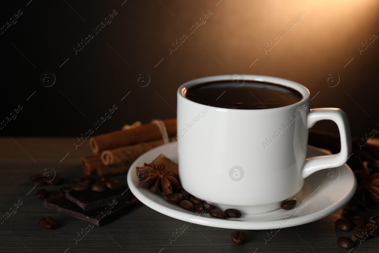 Photo of Cup of delicious hot chocolate, spices and coffee beans on wooden table. Space for text