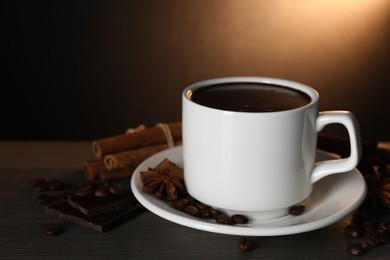 Photo of Cup of delicious hot chocolate, spices and coffee beans on wooden table. Space for text