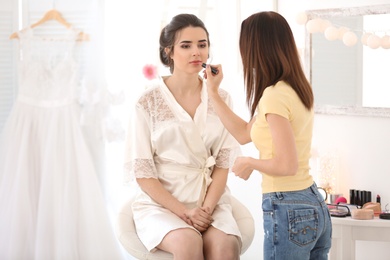 Photo of Professional makeup artist working with young bride in salon