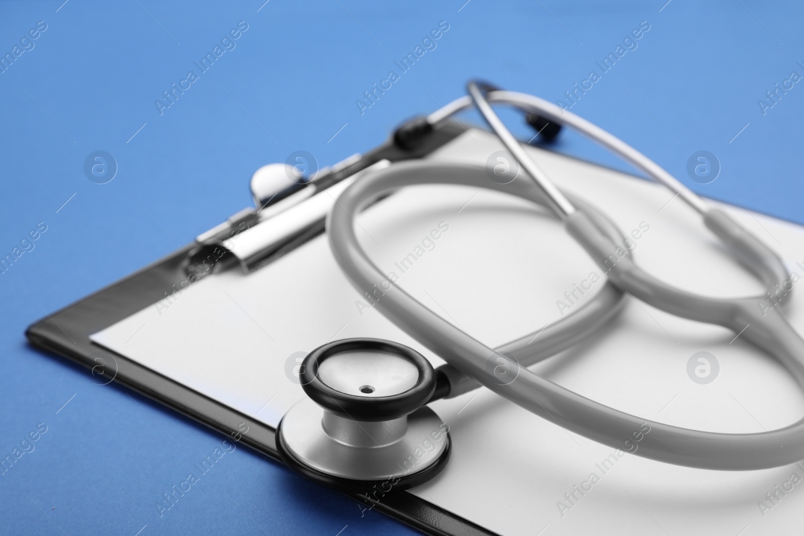 Photo of Clipboard with stethoscope on blue background, closeup