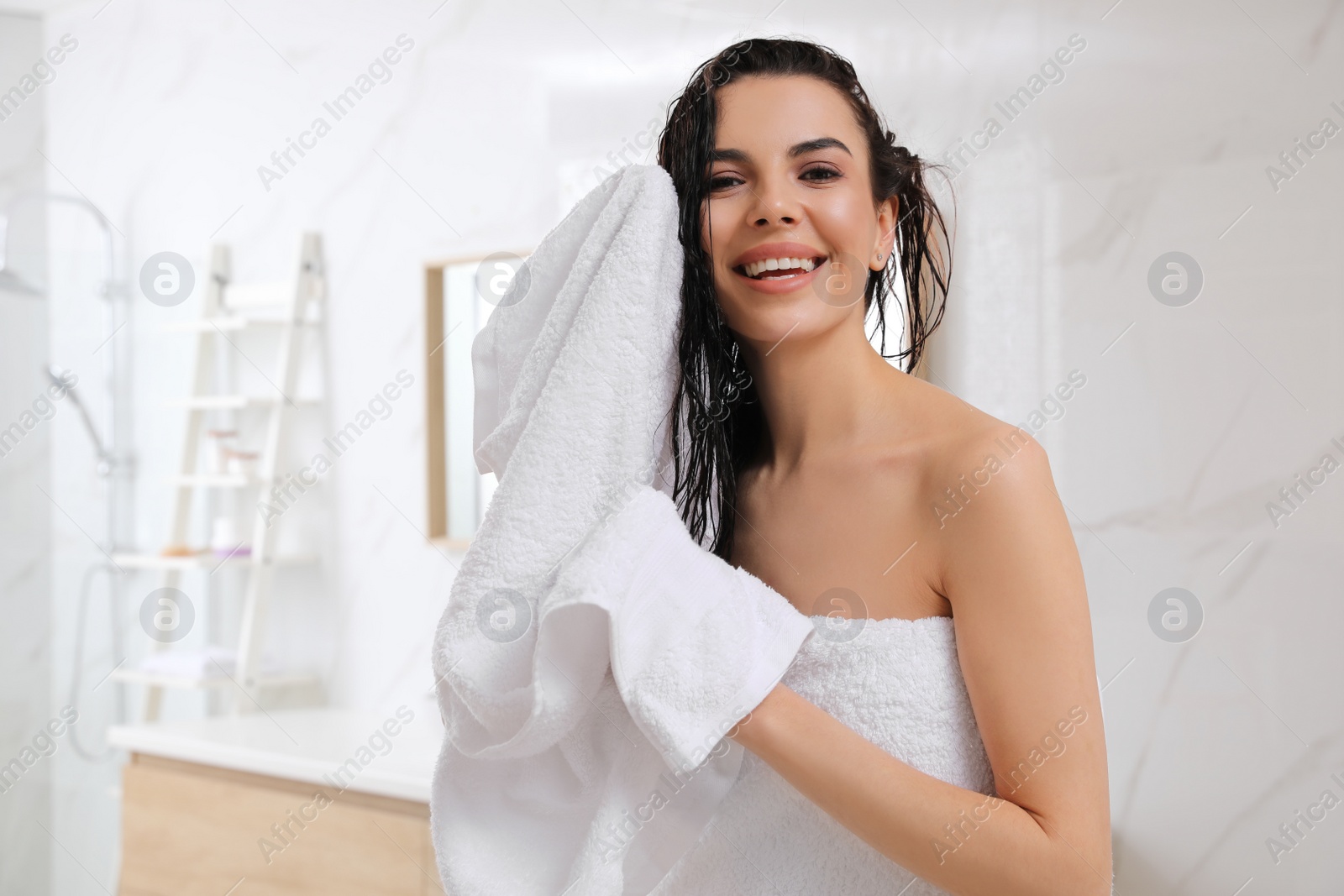 Photo of Happy young woman drying hair with towel after washing in bathroom