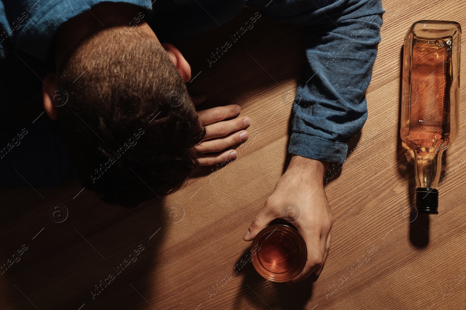 Photo of Addicted man with alcoholic drink at wooden table, top view