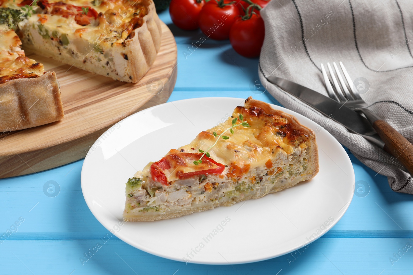 Photo of Piece of tasty quiche with chicken, vegetables, microgreens and cheese on light blue wooden table, closeup