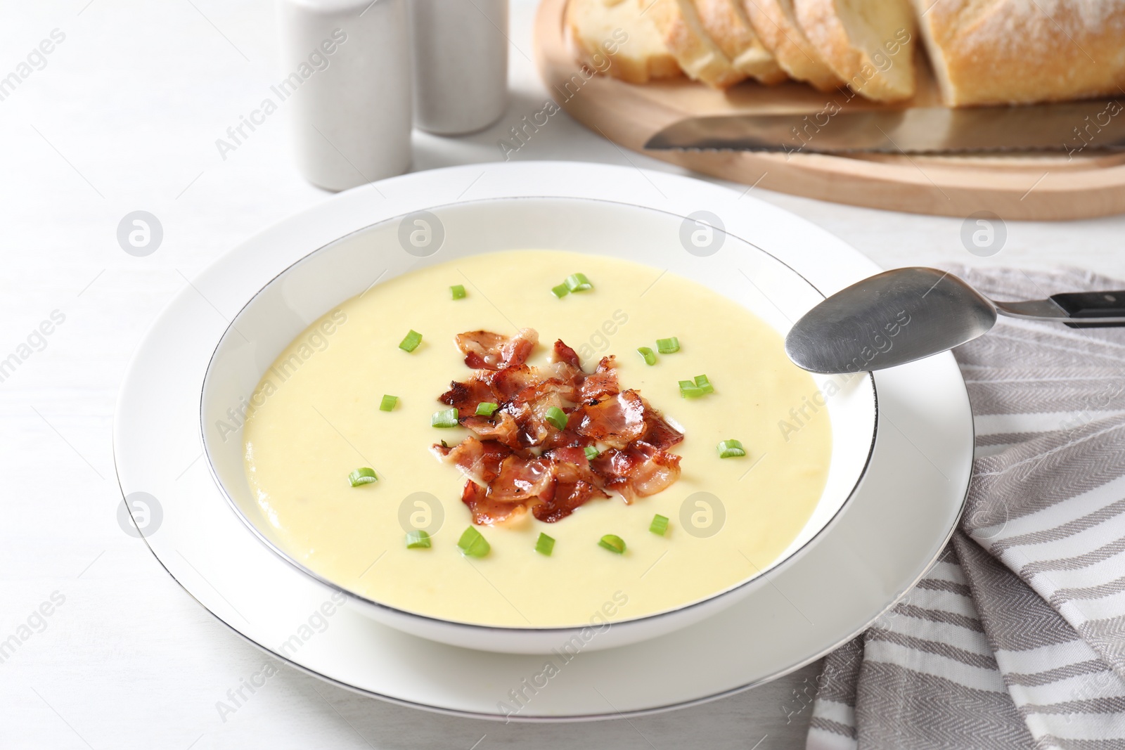 Photo of Tasty potato soup with bacon in bowl and spoon on white table