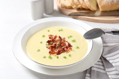 Photo of Tasty potato soup with bacon in bowl and spoon on white table