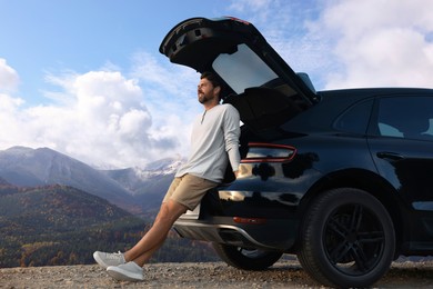 Image of Happy man sitting in trunk of modern car in mountains