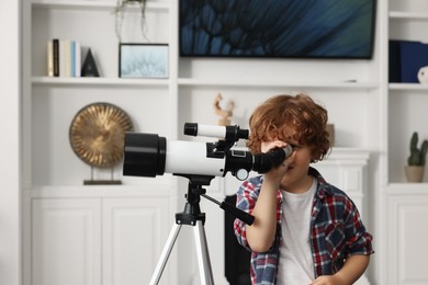 Photo of Cute little boy looking at stars through telescope in room