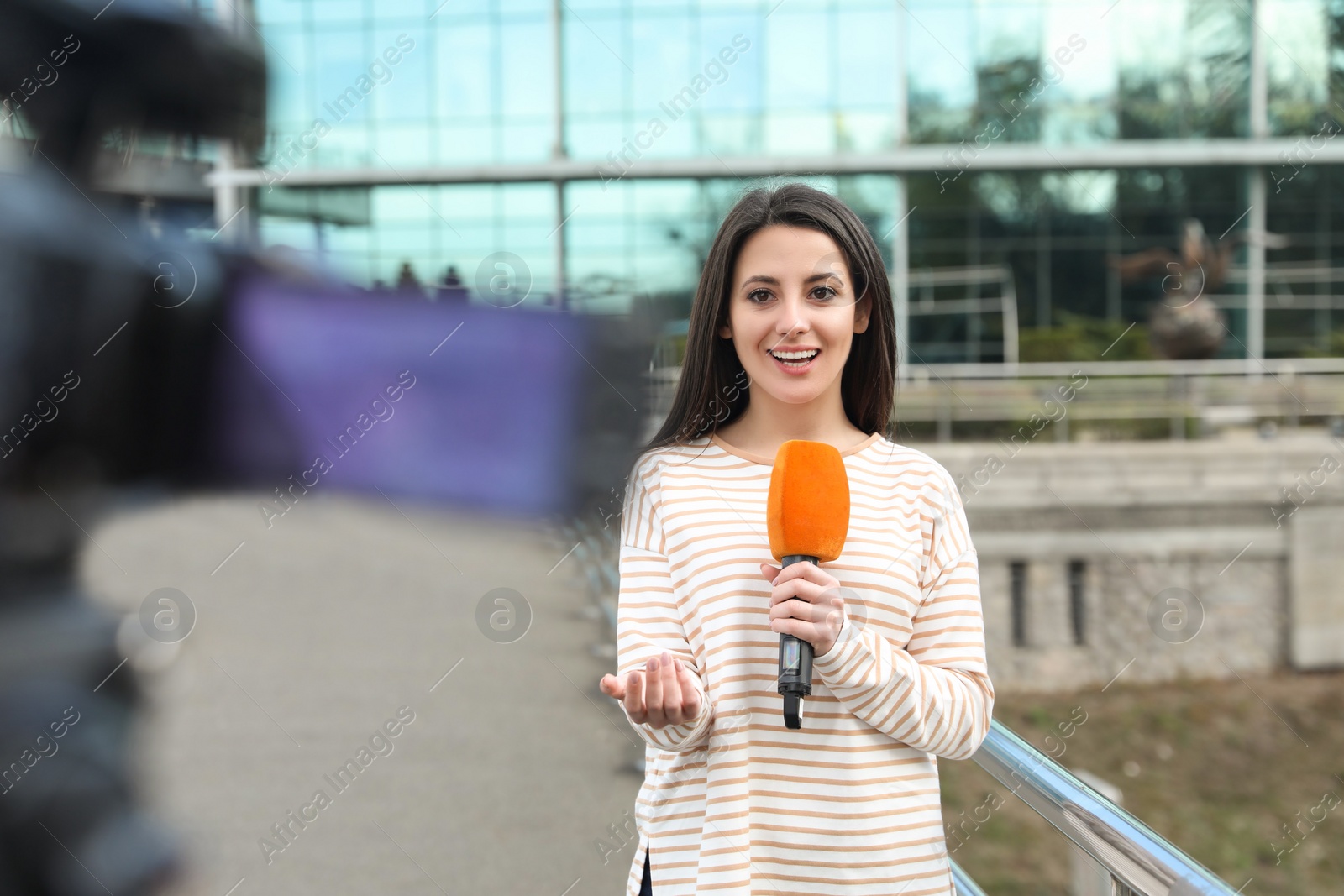 Photo of Young female journalist with microphone working on city street