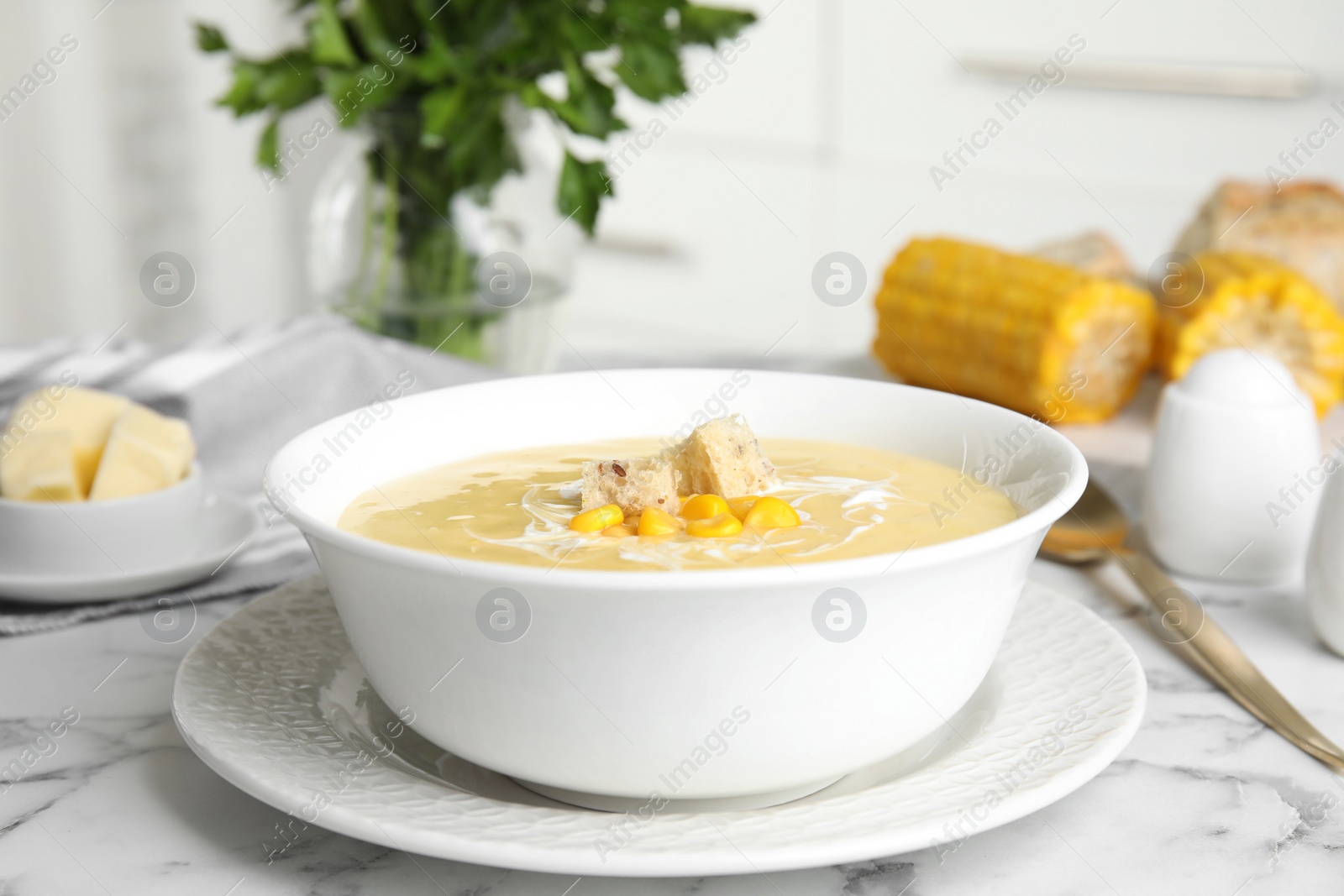 Photo of Delicious corn cream soup served on white marble table indoors