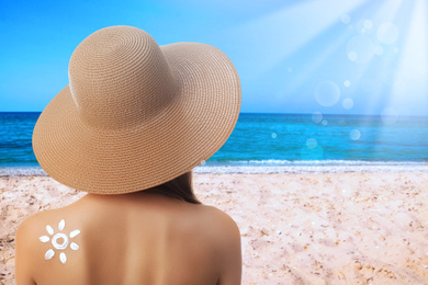 Woman with sun protection cream on her back at beach, space for text