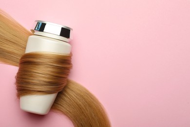Bottle wrapped in lock of hair on pink background, top view with space for text. Natural cosmetic product