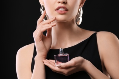 Photo of Beautiful young woman with bottle of perfume on black background, closeup