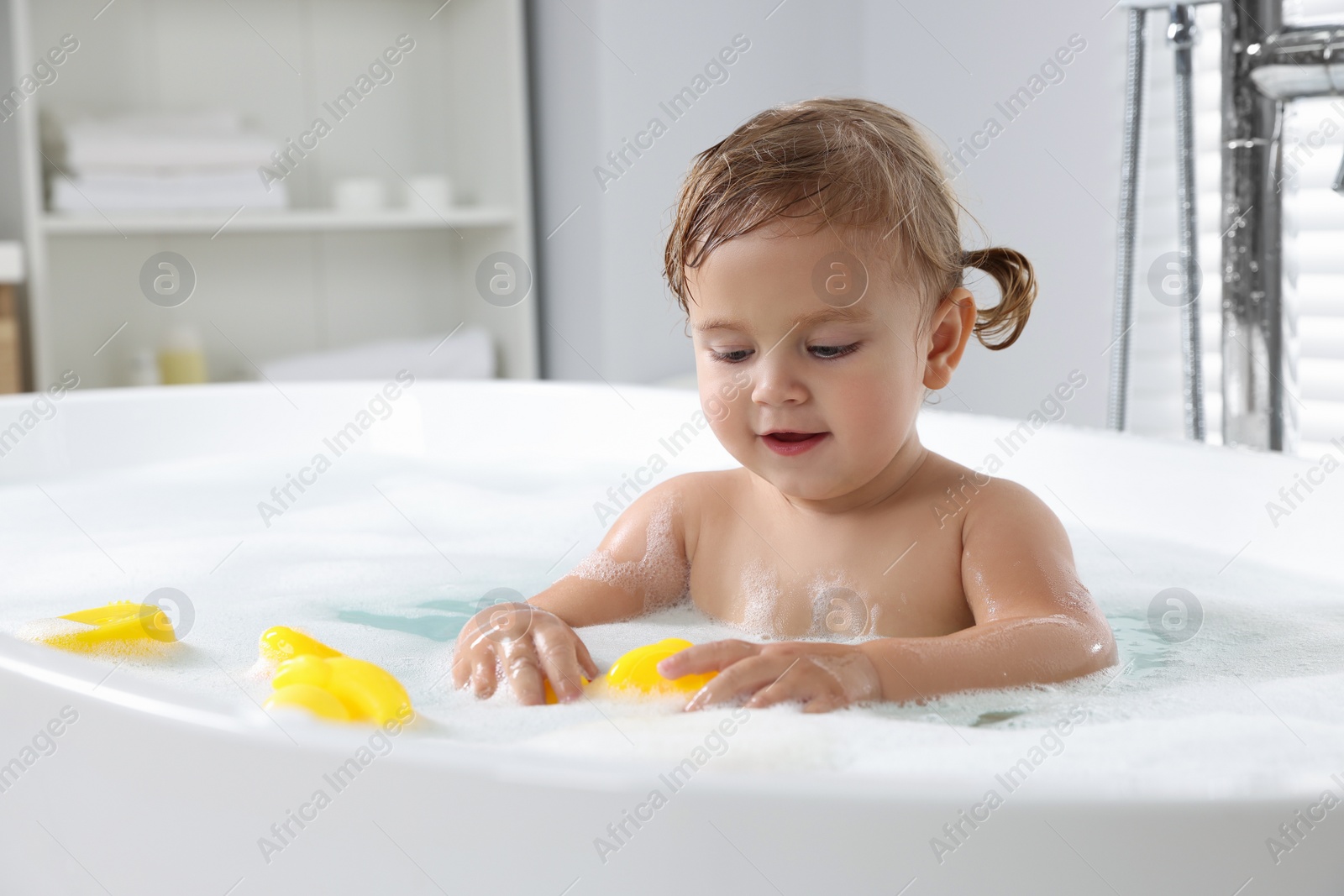 Photo of Cute little girl with rubber ducks in foamy bath at home