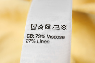 Photo of Clothing label with care symbols and material content on yellow shirt, closeup view
