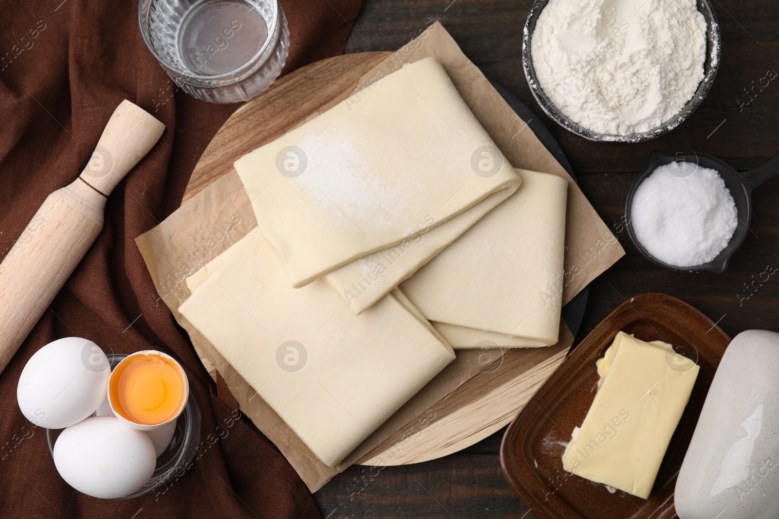 Photo of Raw puff pastry dough and ingredients on wooden table, flat lay