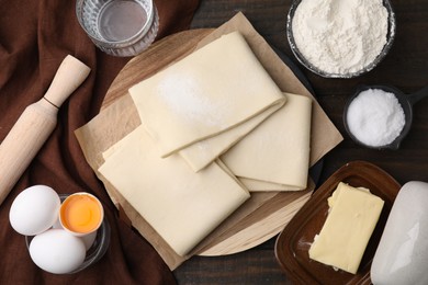 Photo of Raw puff pastry dough and ingredients on wooden table, flat lay