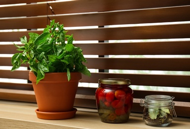 Photo of Green basil, pickled tomatoes and spices on window sill indoors