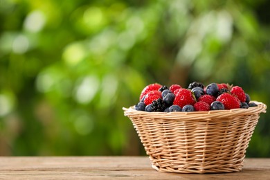 Photo of Wicker bowl with different fresh ripe berries on wooden table outdoors, space for text