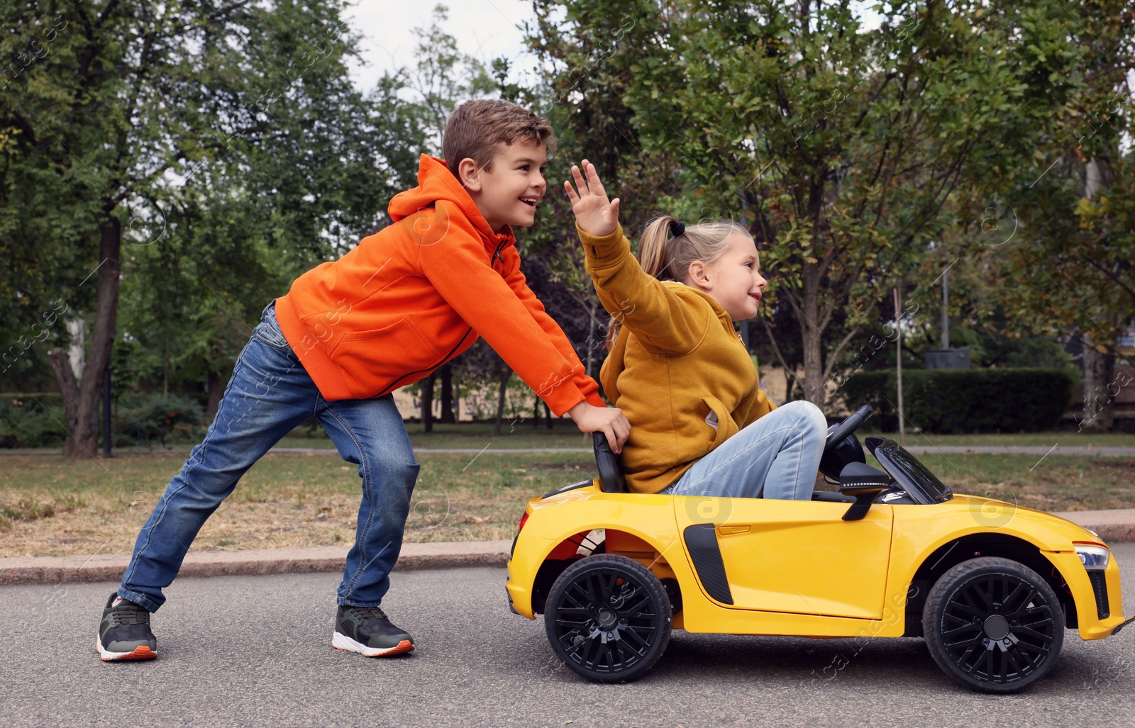 Photo of Cute boy pushing children's car with little girl outdoors