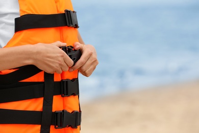 Photo of Female lifeguard putting on life vest near sea, closeup