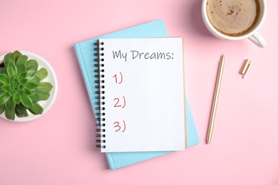 Image of Notebook with dreams list on pink table, flat lay 