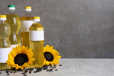 Bottles of sunflower cooking oil, seeds and yellow flowers on light grey table, space for text